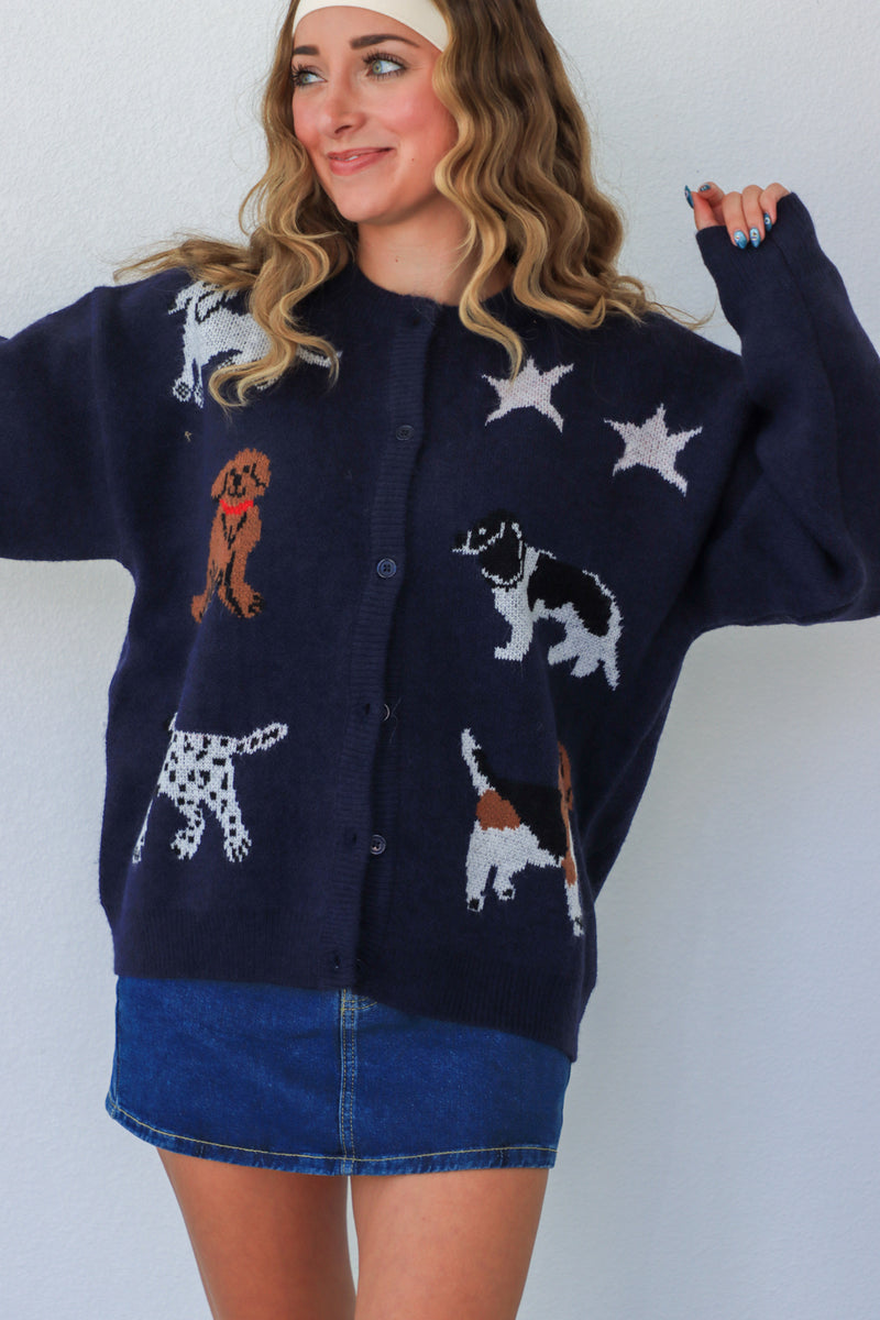 Woman wearing a navy blue cardigan with dog and star patterns against a white background