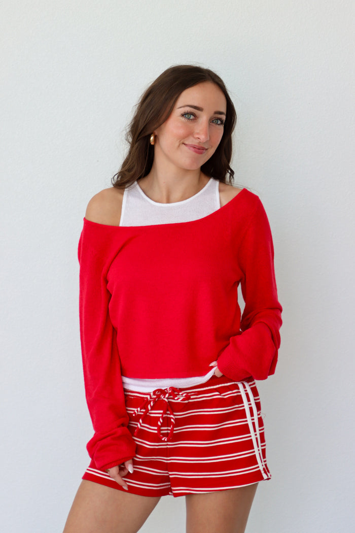 Woman wearing a red off-shoulder top and red and white striped shorts against a white background