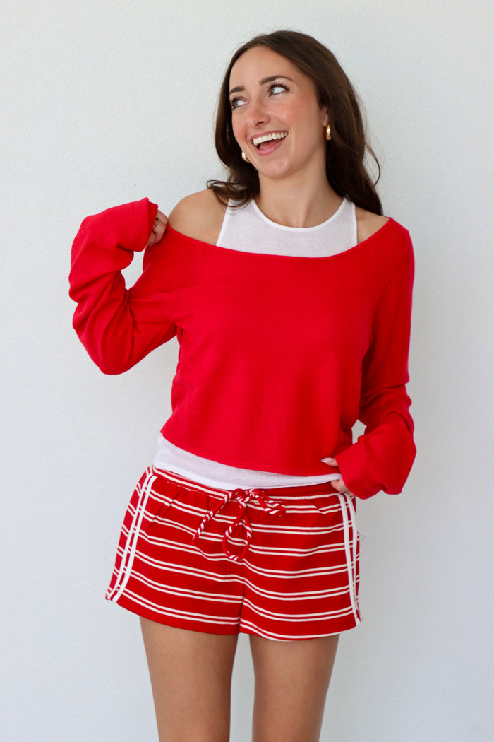 Woman wearing a red sweater and red and white striped short against a white background