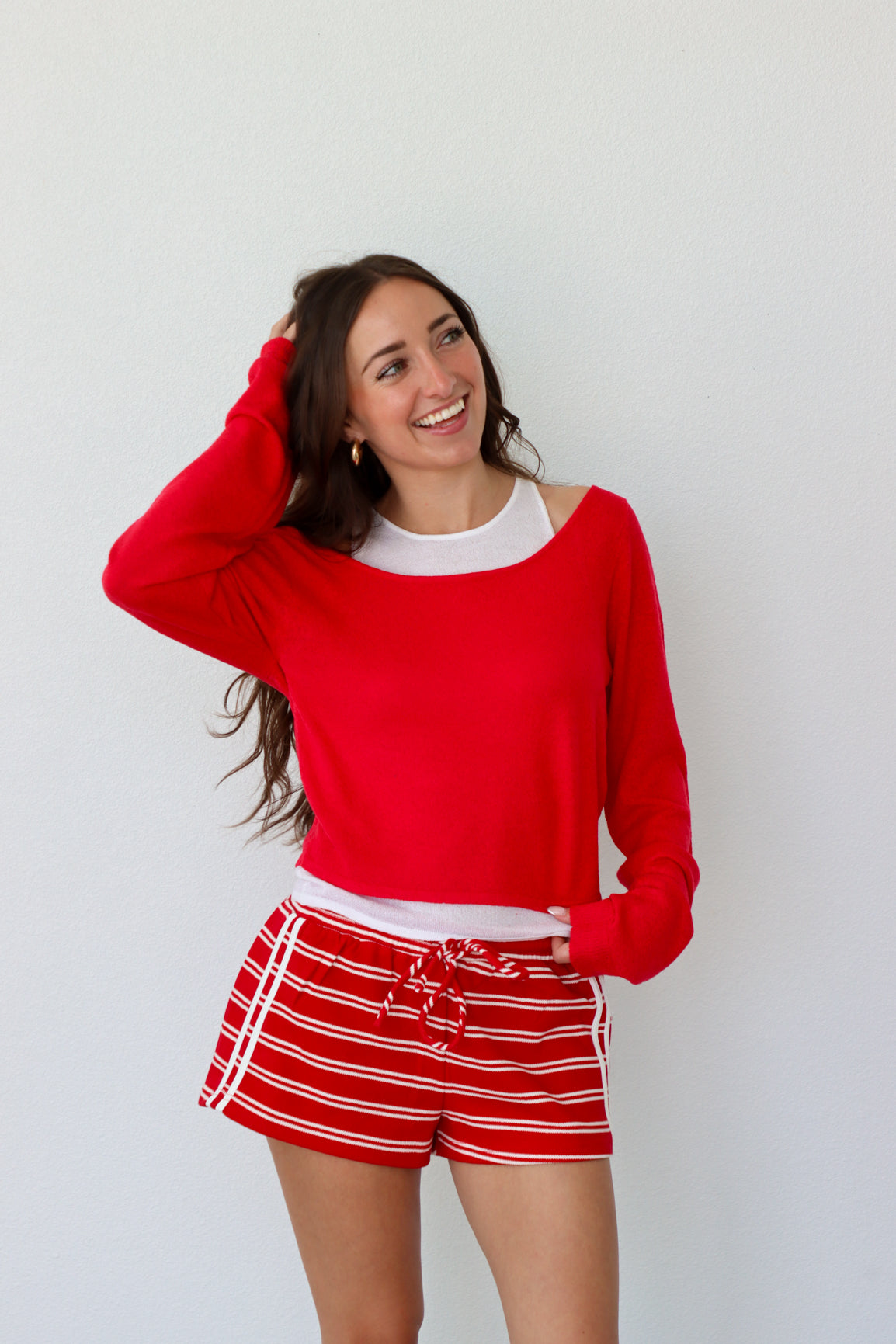 Woman wearing a red sweater and red and white striped shorts against a white background
