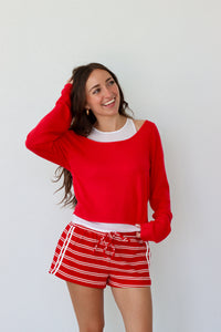 Woman wearing a red sweater and red and white striped shorts against a white background