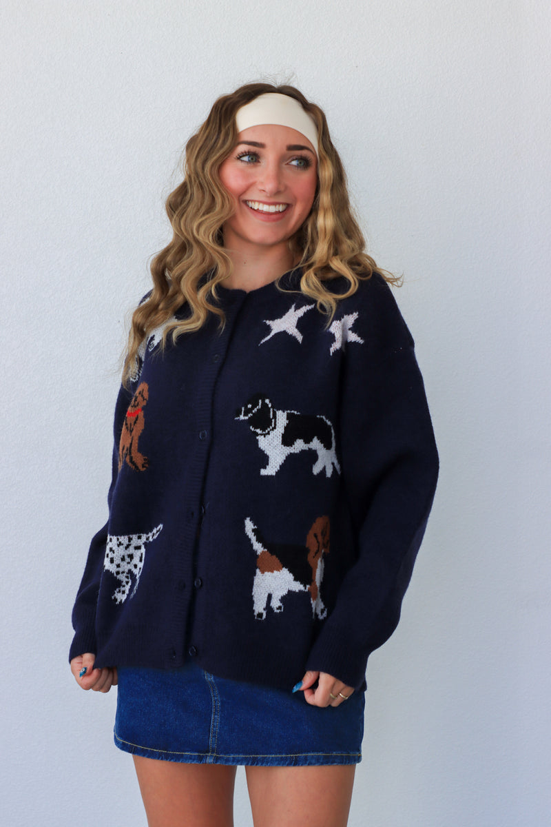 Woman wearing a navy blue cardigan with dog and star patterns against a white background