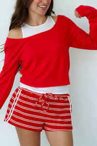 Woman wearing a red long-sleeve top and red and white striped shorts against a white background
