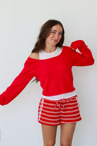 Woman wearing a red sweater and striped shorts against a white background