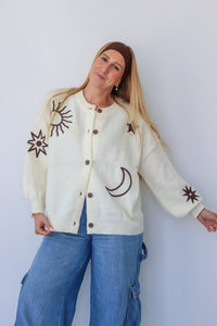 Woman wearing a cream cardigan with embroidered designs against a white background