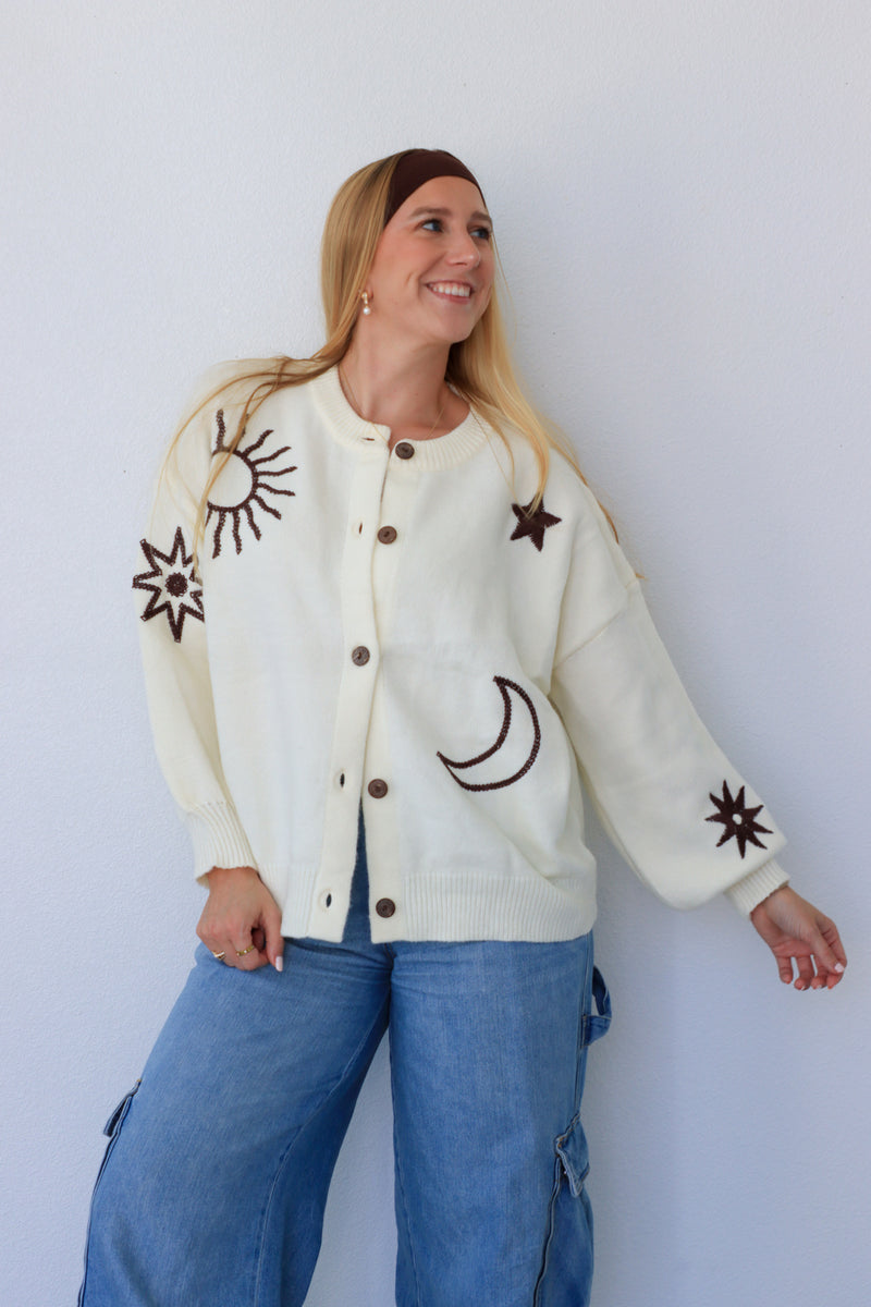 Woman wearing a cream cardigan with star and moon designs against a white background