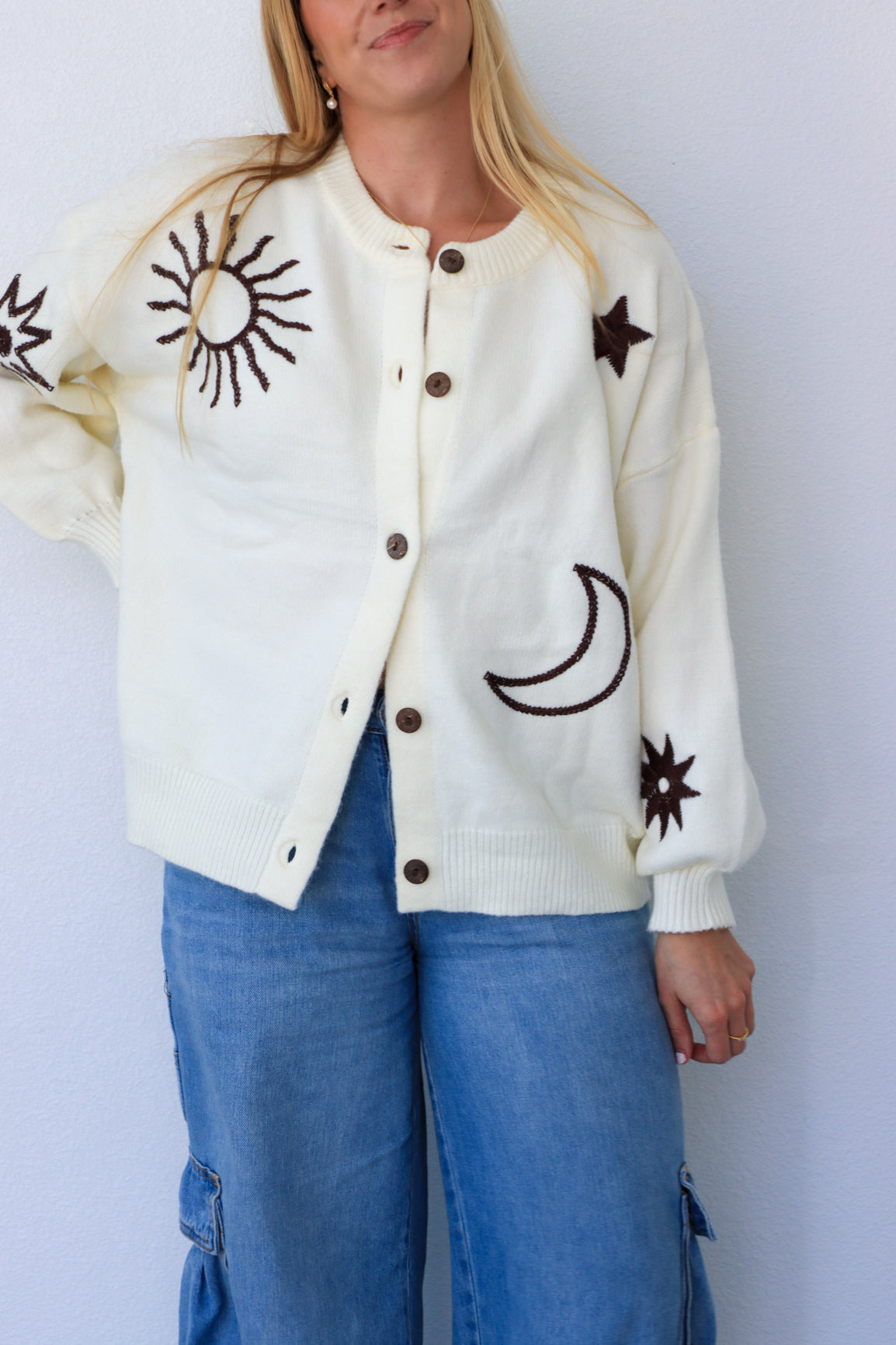 Person wearing a cream cardigan with black sun and moon designs on a white background