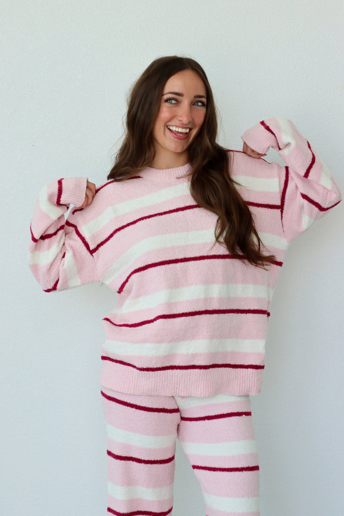 Woman wearing a pink and white striped sweater and pants against a plain background