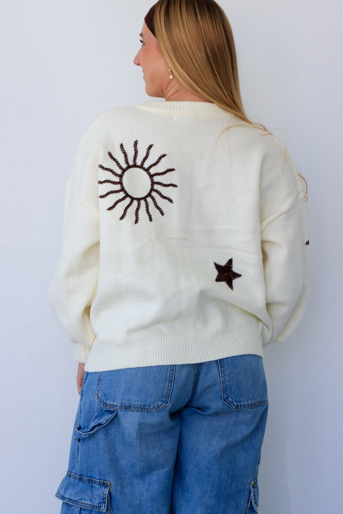 Person wearing a cream sweater with a sun design on the back, standing against a white background