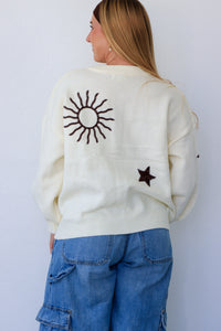 Person wearing a cream sweater with a sun design on the back, standing against a white background