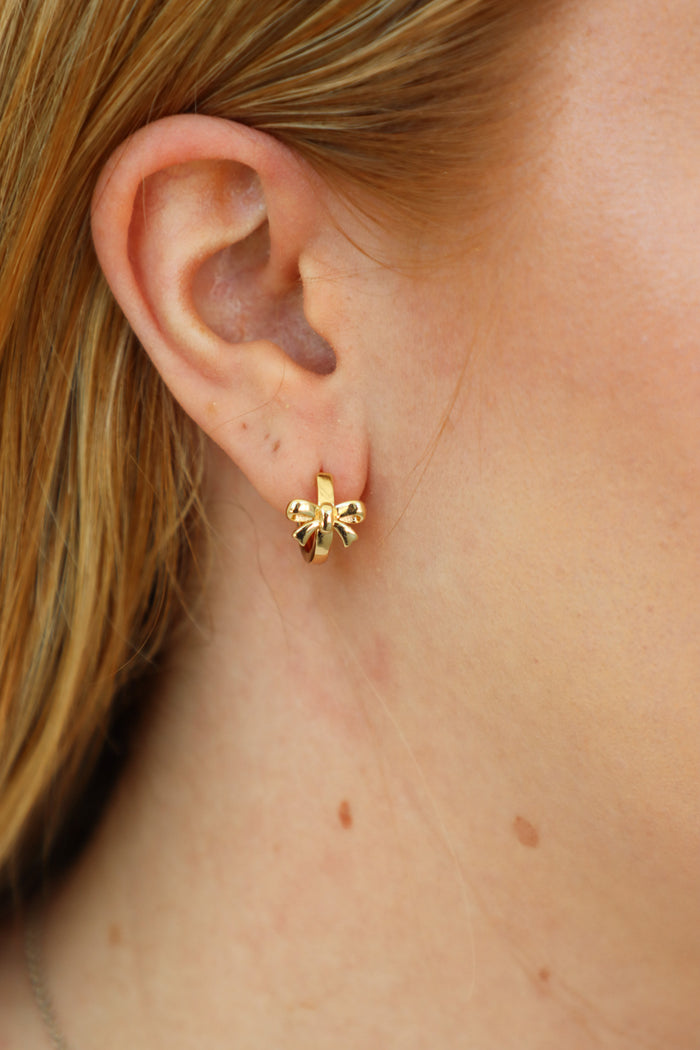 girl wearing gold bow huggie hoop earrings
