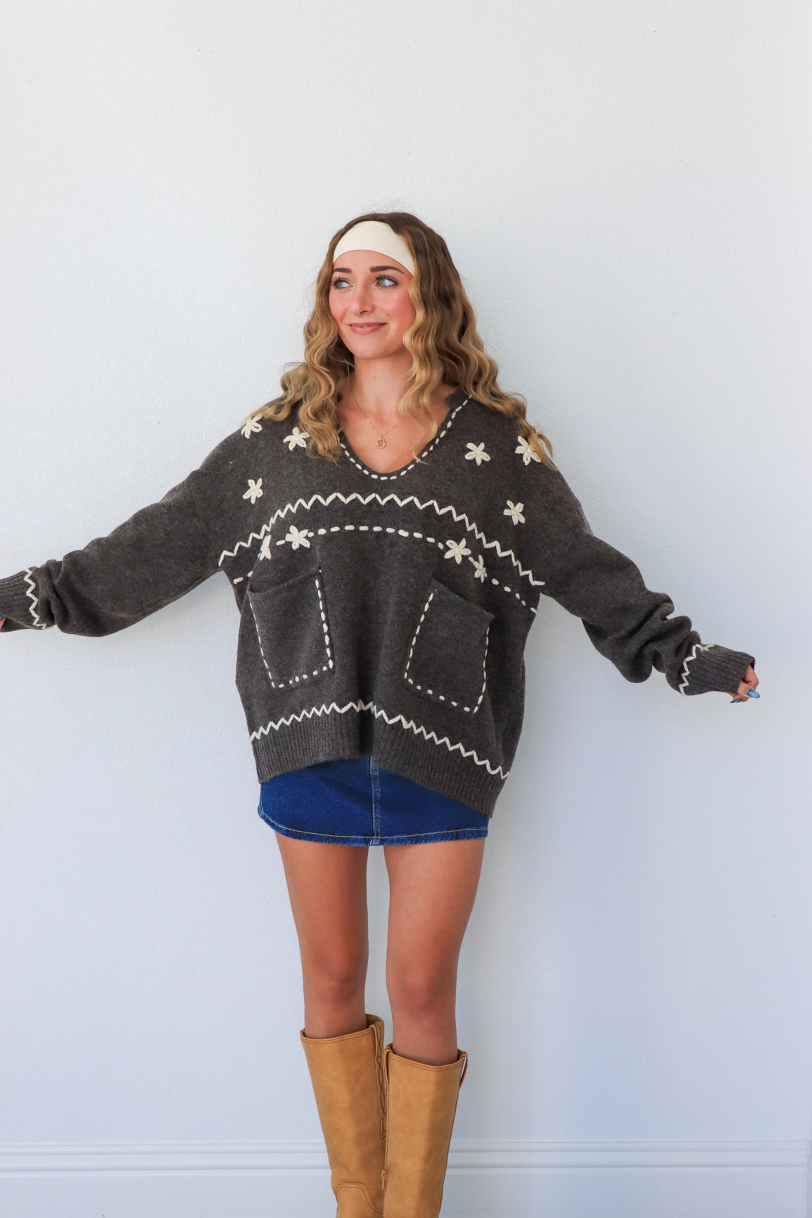 Woman wearing a dark gray sweater with white patterns, blue shorts, and brown boots against a light background