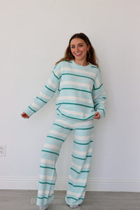 Woman wearing a light blue and white striped set against a plain white wall.