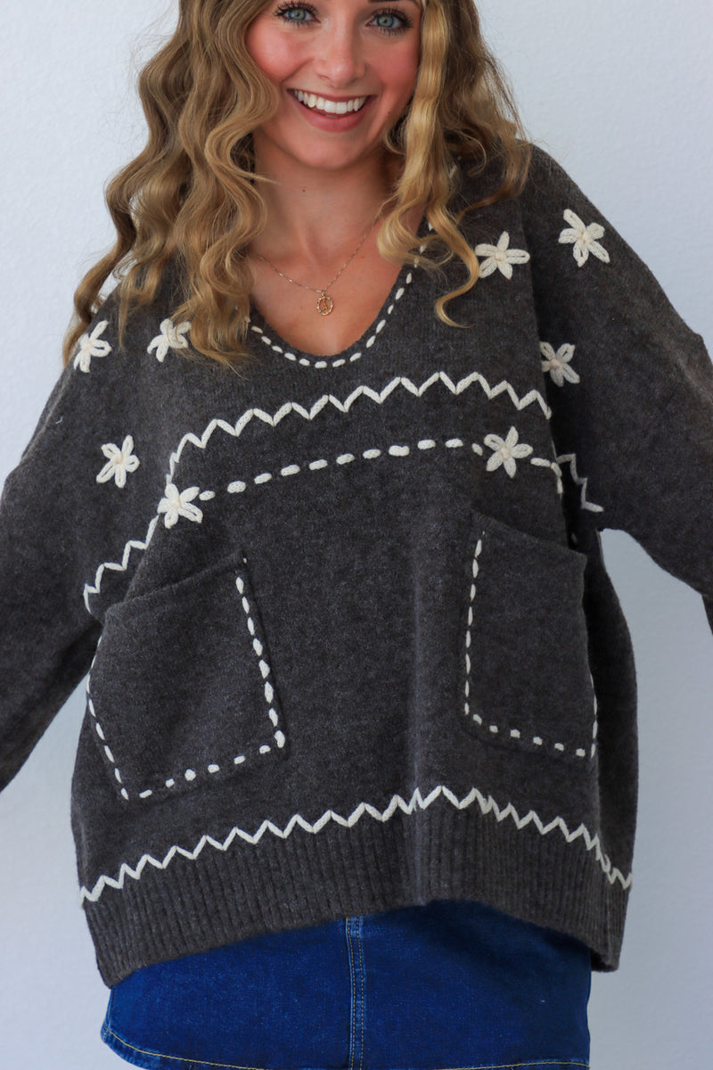 Woman wearing a dark gray sweater with white patterns against a plain background