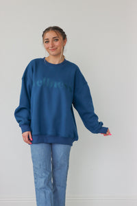 girl wearing teal crewneck with "wellness" embroidered graphic