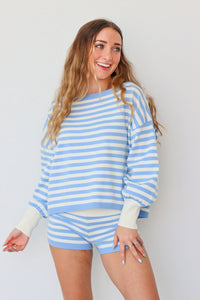 Woman wearing a blue and white striped sweater and shorts against a plain background