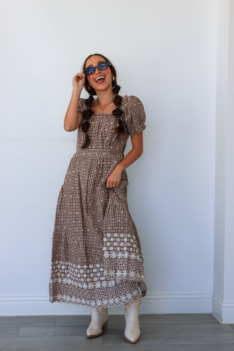 Woman wearing a patterned dress and white boots against a plain wall.