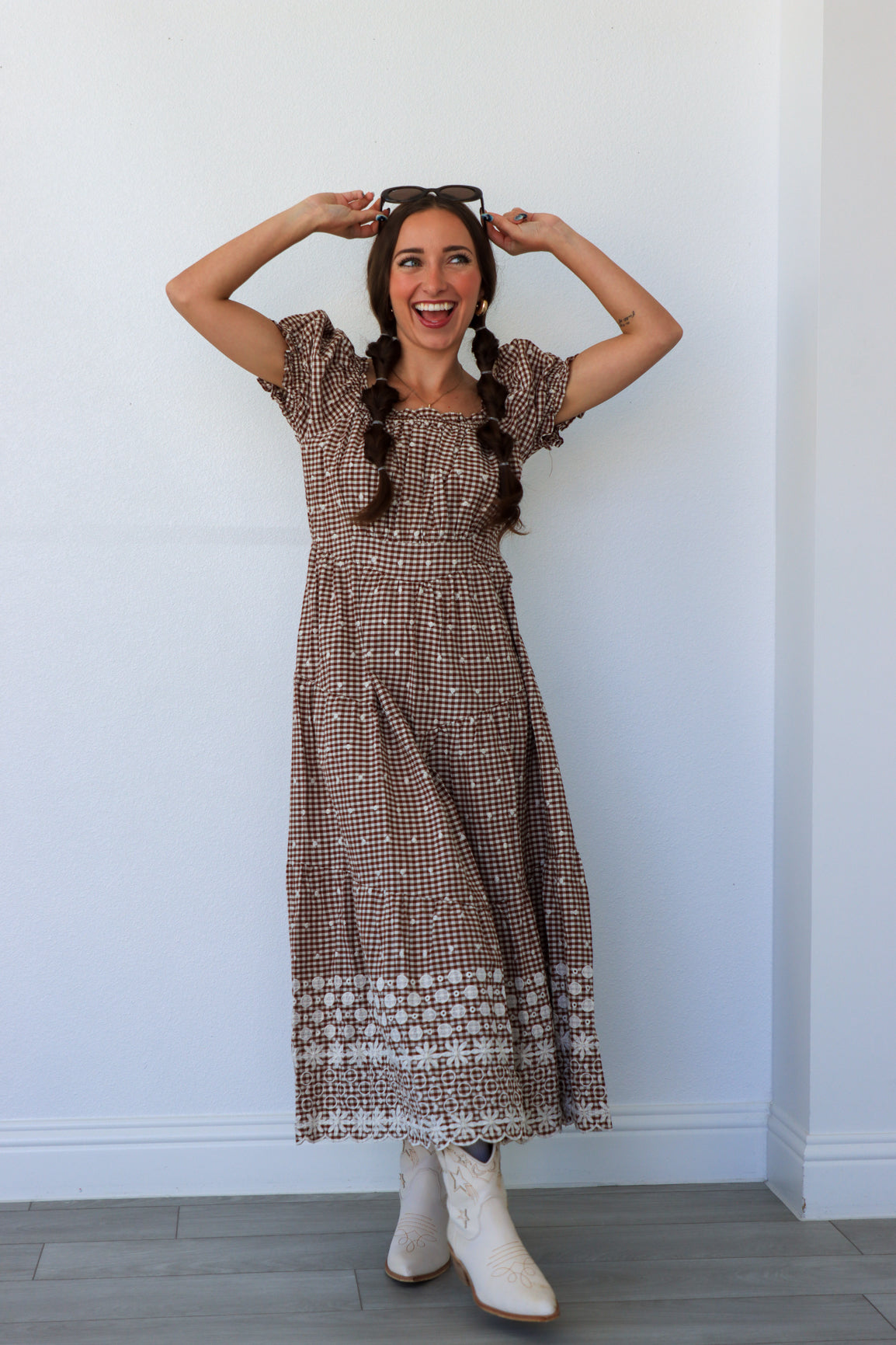 Woman wearing a patterned dress and white boots against a plain wall.