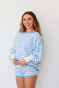 Woman wearing a blue and white striped sweater and shorts against a plain background