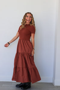 Woman wearing a rust-colored dress standing against a white wall.