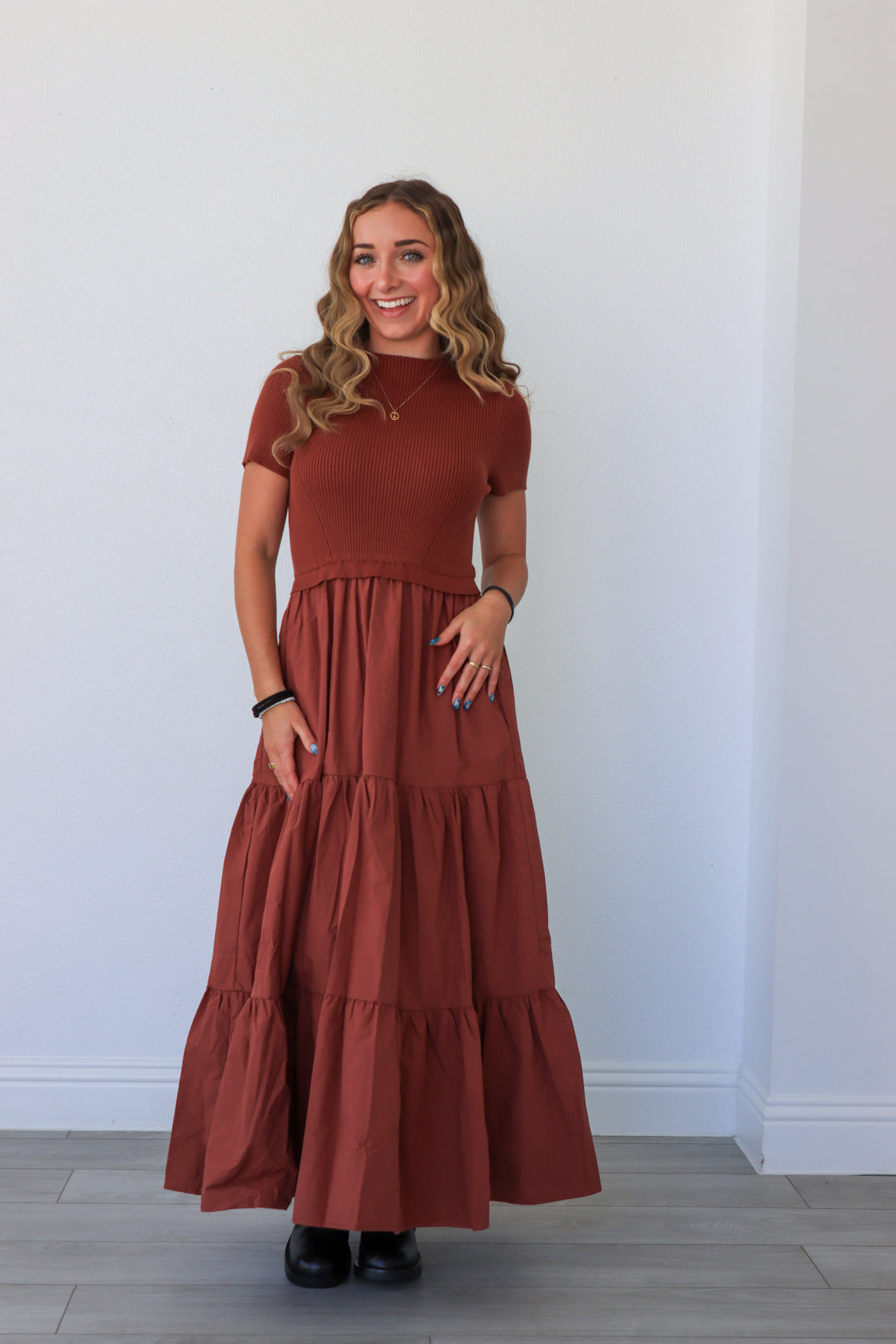 Woman wearing a long rust-colored dress against a white wall.