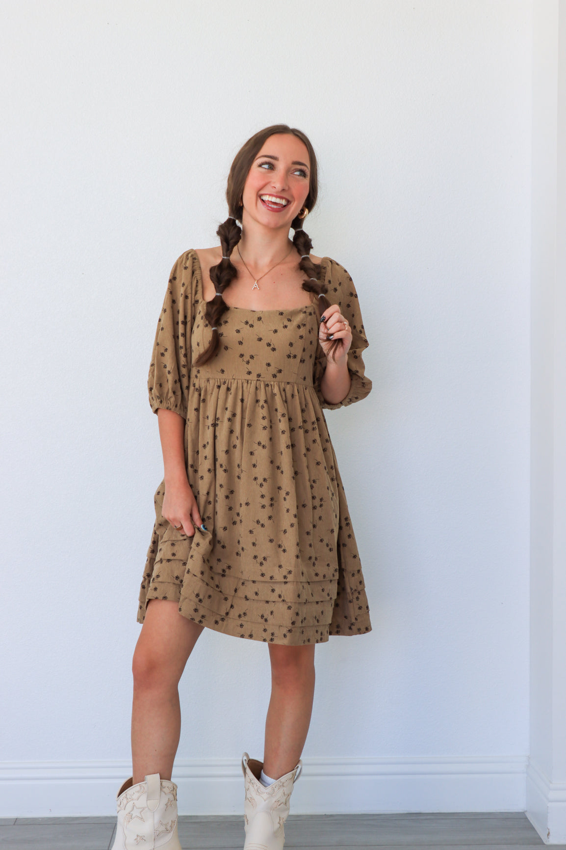 Woman wearing a patterned dress with white boots against a white wall