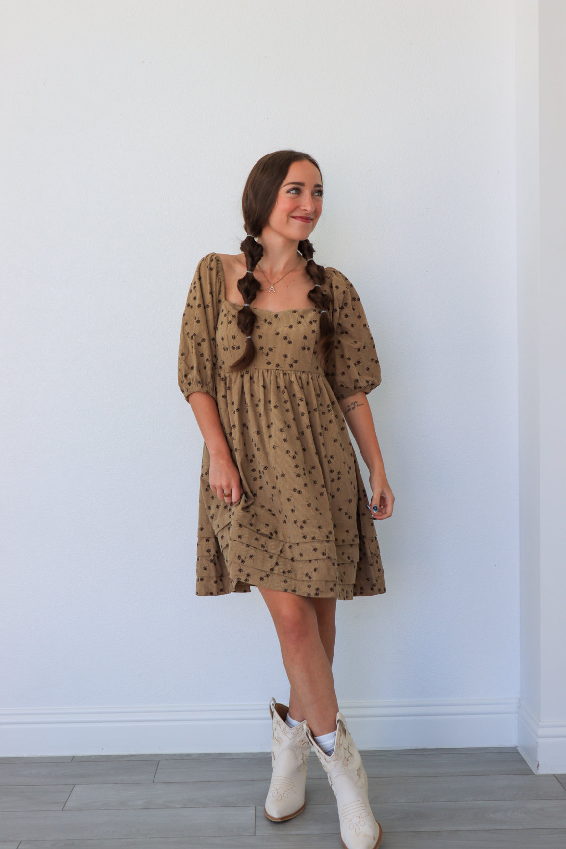 Woman wearing a patterned dress and white boots against a plain background