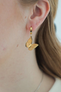 girl wearing gold butterfly huggie hoop earrings