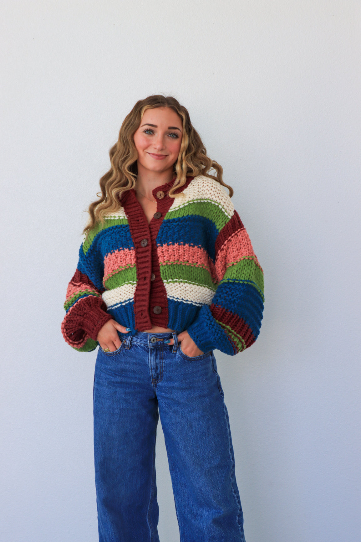 Person wearing a colorful striped sweater and blue jeans against a white background