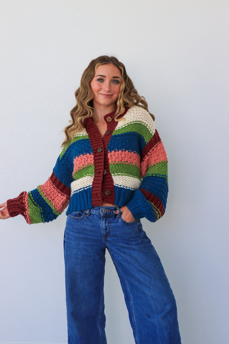 Person wearing a colorful striped cardigan and blue jeans against a white background