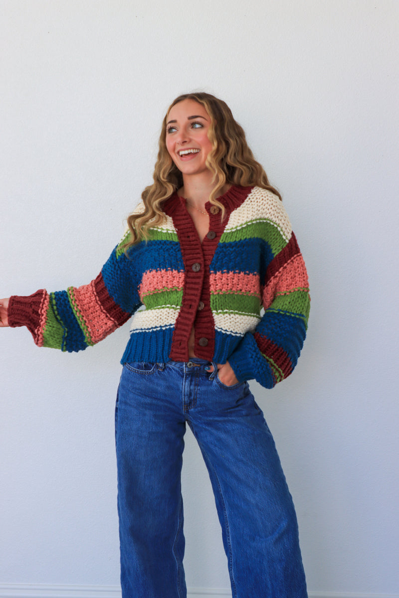Person wearing a colorful striped sweater and blue jeans against a white background