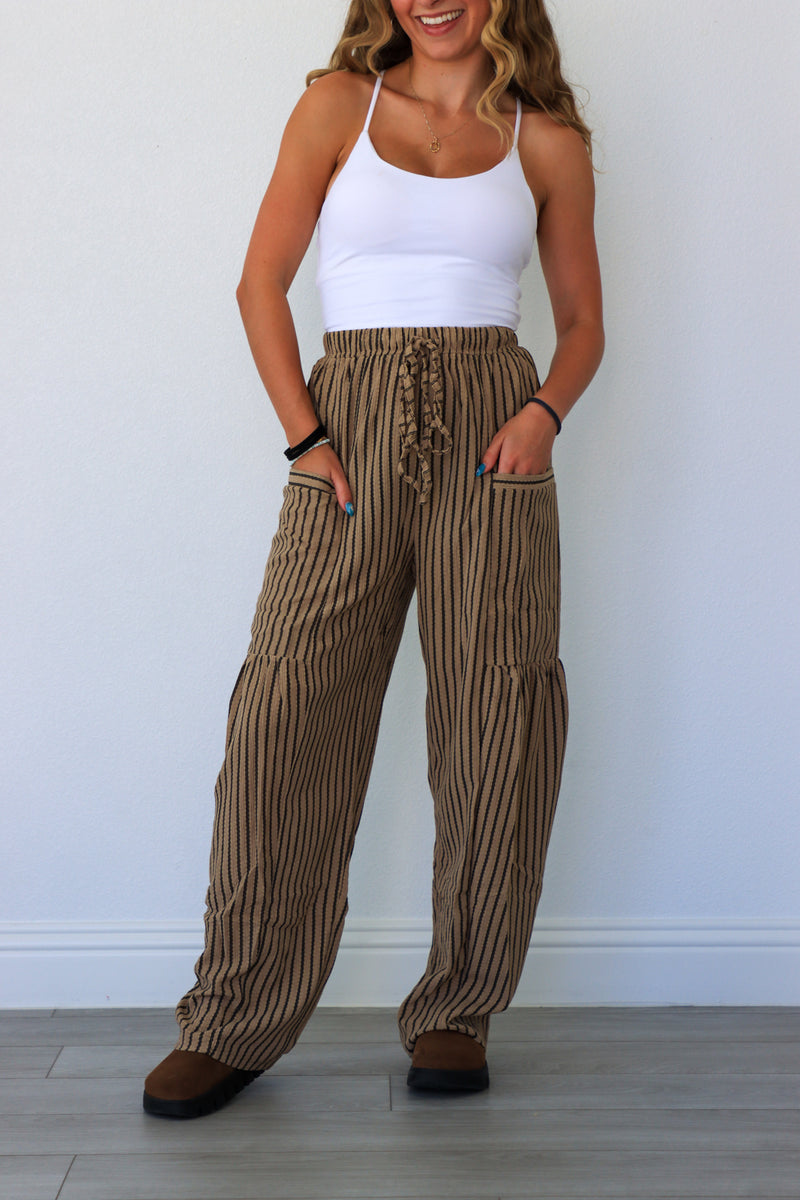 Woman wearing a white tank top and brown striped pants against a white background