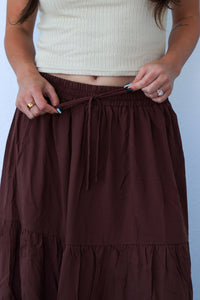 Brown tiered skirt worn by a person against a light blue background