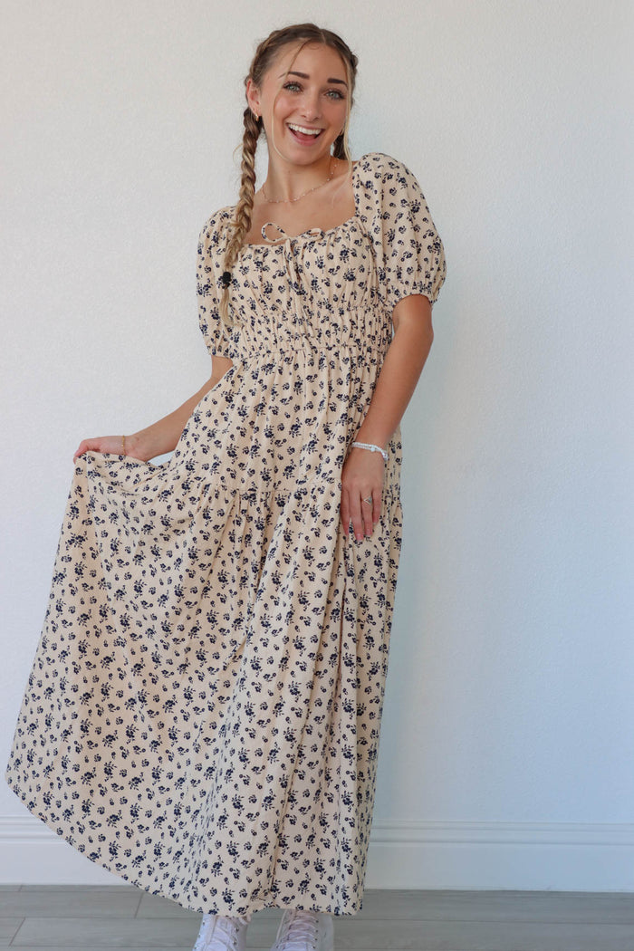girl wearing cream long dress with navy floral pattern and puffed sleeves