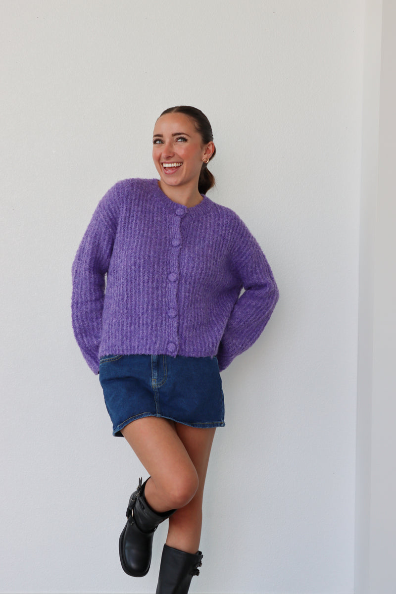 Woman wearing a purple sweater and denim skirt against a white background