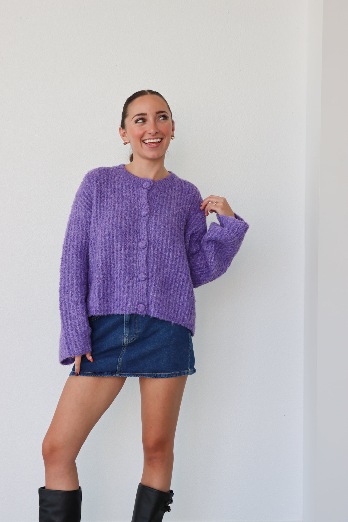 Woman wearing a purple sweater and denim skirt against a white background