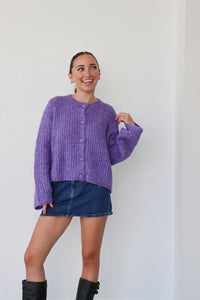 Woman wearing a purple sweater and denim skirt against a white background