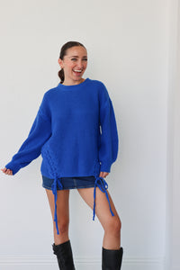 Woman wearing a blue sweater and denim skirt with black knee-high boots against a white background