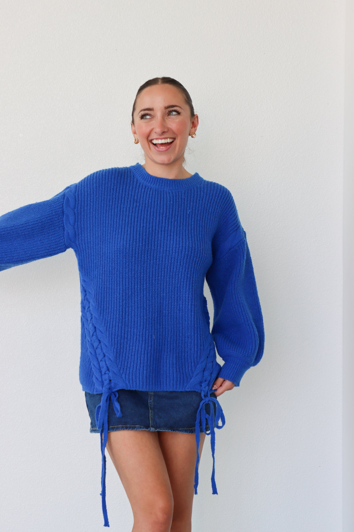 Person wearing a blue sweater and denim skirt against a white background