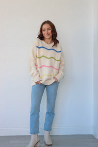 girl wearing cream knit sweater with blue, green, pink, and yellow knit stripe detailing