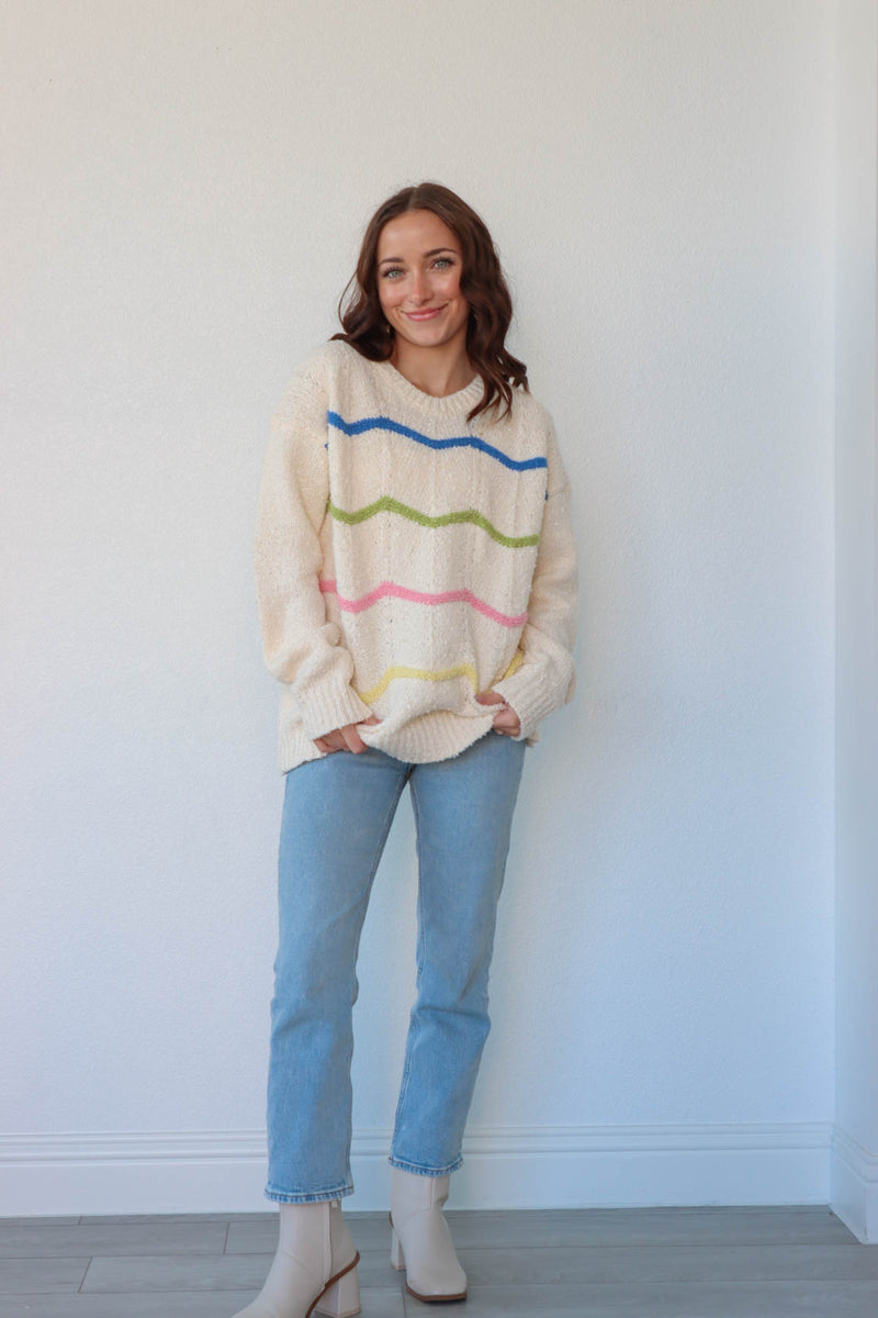 girl wearing cream knit sweater with blue, green, pink, and yellow knit stripe detailing