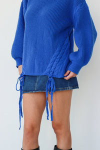 Person wearing a blue sweater and denim skirt with a white background