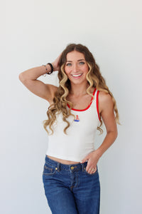 Woman wearing a white tank top with red trim and blue jeans against a white background