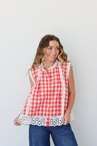 Woman wearing a red and white checkered sleeveless top with lace trim against a plain background