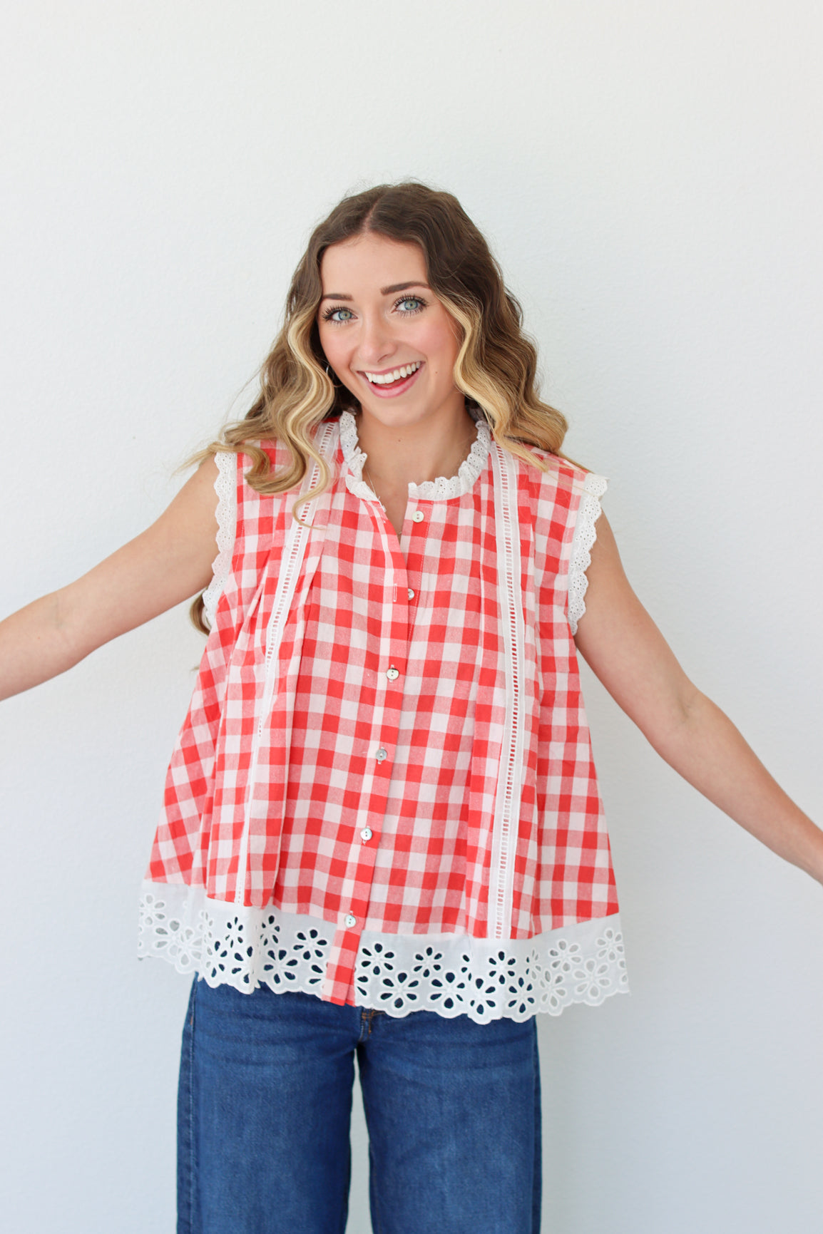 Woman wearing a red and white checkered sleeveless top with lace trim against a plain background