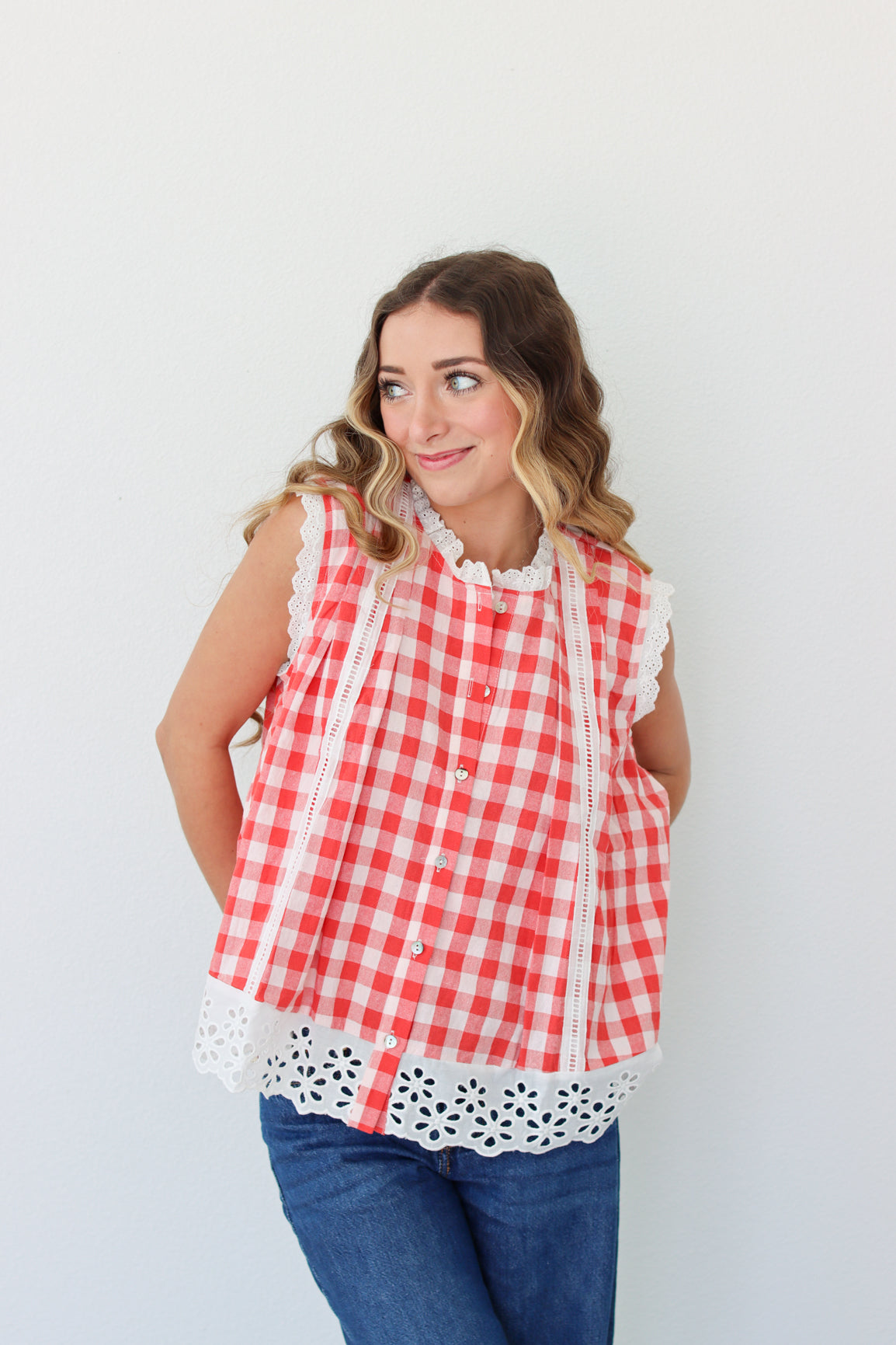 Woman wearing a red and white checkered top with lace details against a plain background