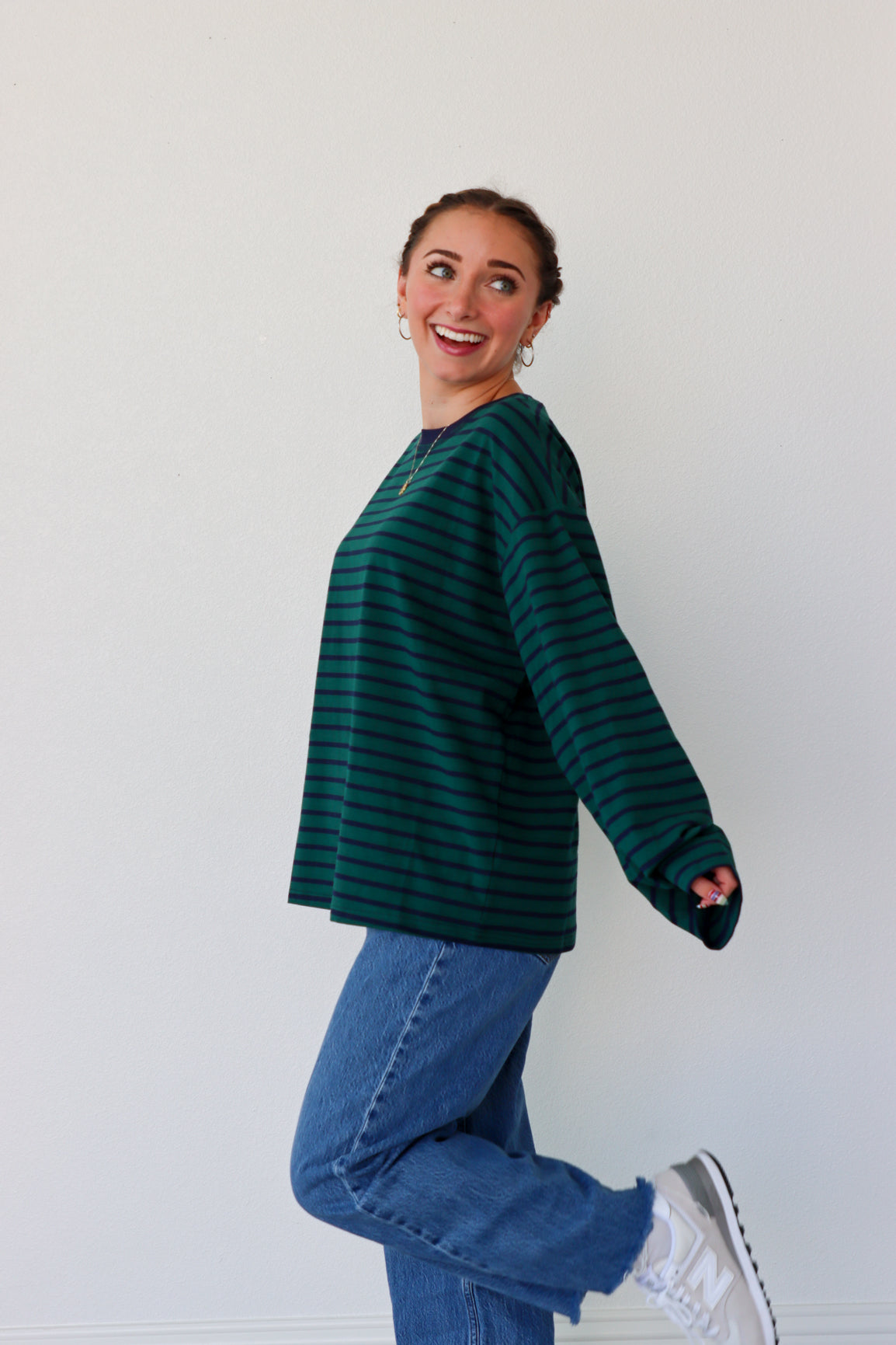 Person wearing a green striped sweater and blue jeans against a white background