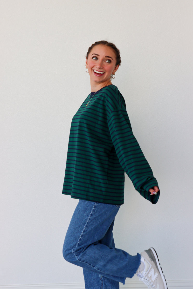 Person wearing a green striped sweater and blue jeans against a white background