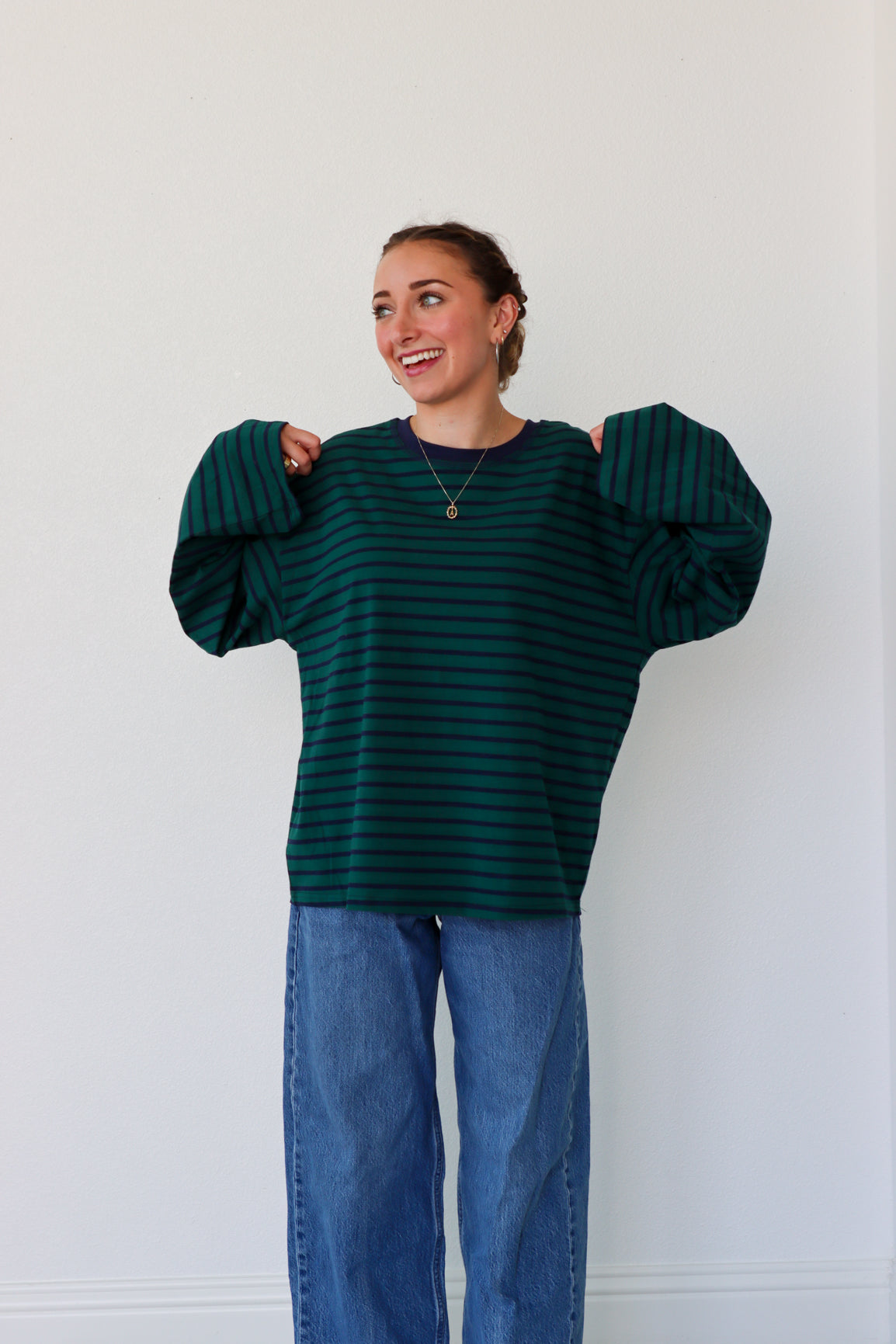 Person wearing a green striped sweater and blue jeans against a white wall