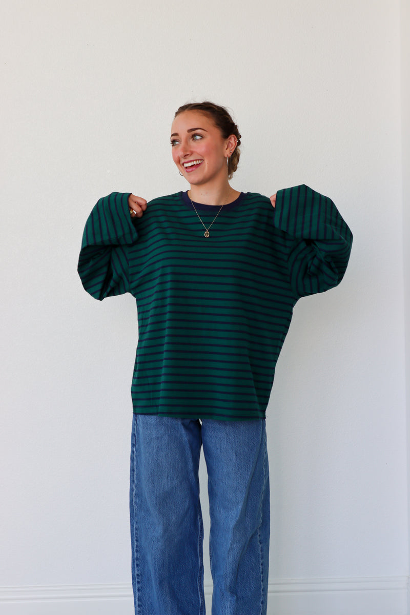 Person wearing a green striped sweater and blue jeans against a white wall